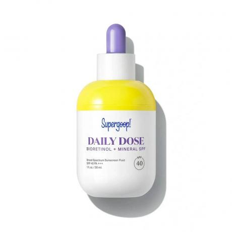 Egy sárga-fehér üveg Supergoop Daily Dose Bioretinol + Mineral SPF 40 fehér alapon