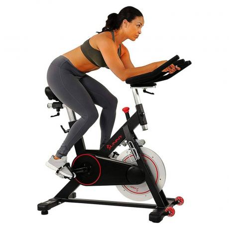 Sunny Health & Fitness Vélo d'intérieur à entraînement par courroie magnétique personne utilisant un vélo d'intérieur sur fond blanc