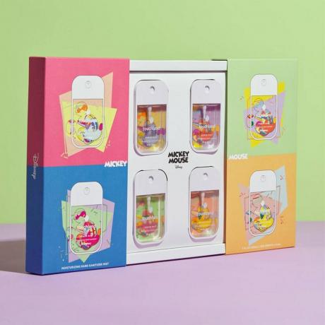 Šiek tiek atidaryta Disney ir Touchland Power Mist rankų dezinfekavimo priemonių kolekcijos dėžutė su keturiais purškimo buteliukais žaliame ir violetiniame fone