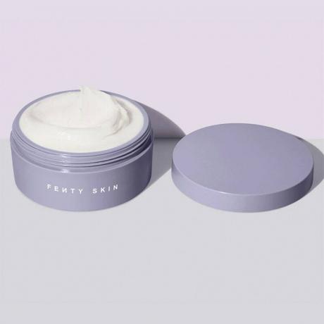 Un pot de lavande de la crème pour le corps Fenty Skin Butta Drop Whipped Oil sur fond violet et gris