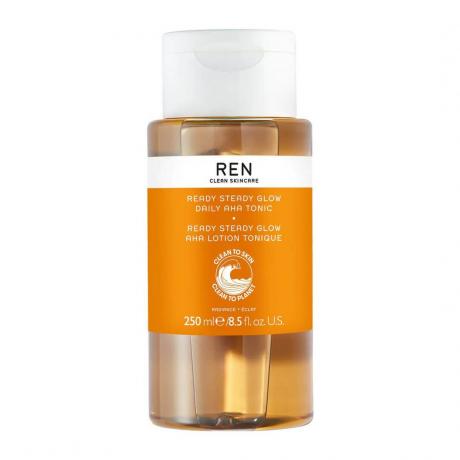 Ren Clean Skincare Ready Steady Glow Daily AHA Tonic prozirna bočica narančastog tonika s narančastom etiketom i bijelim čepom na bijeloj pozadini