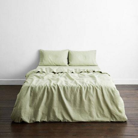 बेड थ्रेड्स 100% फ्रेंच फ्लैक्स लिनन बिस्तर सेट: गहरे भूरे लकड़ी के फर्श और सफेद दीवारों वाले कमरे में हरी चादर वाला एक बिस्तर