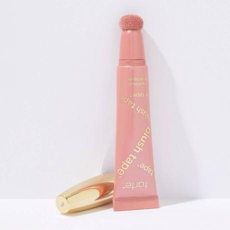 Tarte Blush Tape Liquid Blush ვარდისფერი საწნეხი რუჟის მილი ოქროსფერი თავსახურით გვერდით ღია ნაცრისფერ ფონზე