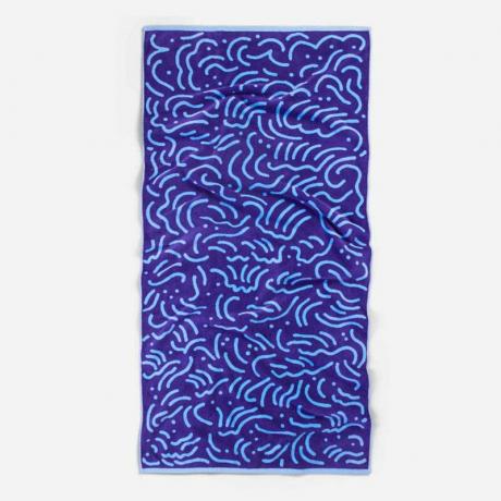 Toalla de playa Brooklinen Artist Series: una toalla de playa azul oscuro con un diseño de garabatos azul claro sobre un fondo gris.