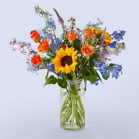 ProFlowers buket žutog, ljubičastog i narančastog cvijeća u prozirnoj vazi na pozadini boje lavande