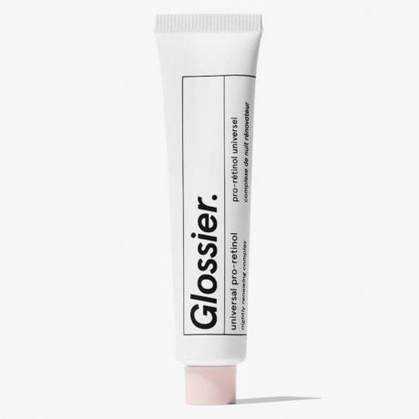 Tabung putih Glossier Mini Universal Pro Retinol dengan tutup merah muda pada latar belakang abu-abu