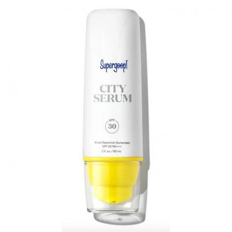 Bela steklenička z rumeno črpalko seruma Supergoop City na belem ozadju