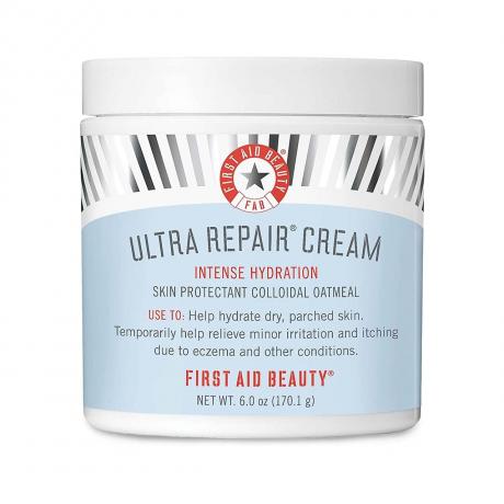 First Aid Beauty Ultra Repair Cream balta burka ar zilu etiķeti, sudraba hroma svītrām un sarkanu tekstu uz balta fona
