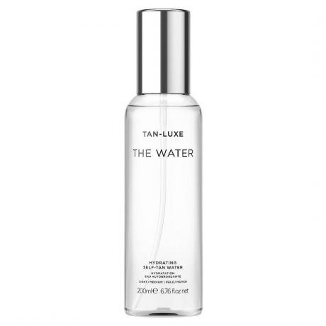 زجاجة Tan-Luxe The Water Hydating Self-Tan Water شفافة مع غطاء فضي على خلفية بيضاء