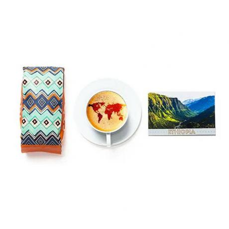 Atlas Coffee Club -tilauskuvioinen kahvipussi, kuppi kahvia maailmankartan latte-taideella ja Etiopia-postikortti valkoisella pohjalla